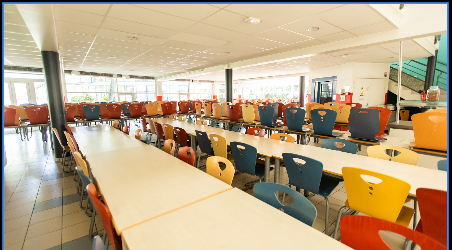 restaurant scolaire 2 Des tables du restaurant sont agencées près des fenêtres et des photos de pommes, poires et tomates avec des smileys dessus sont accrochées au mur.